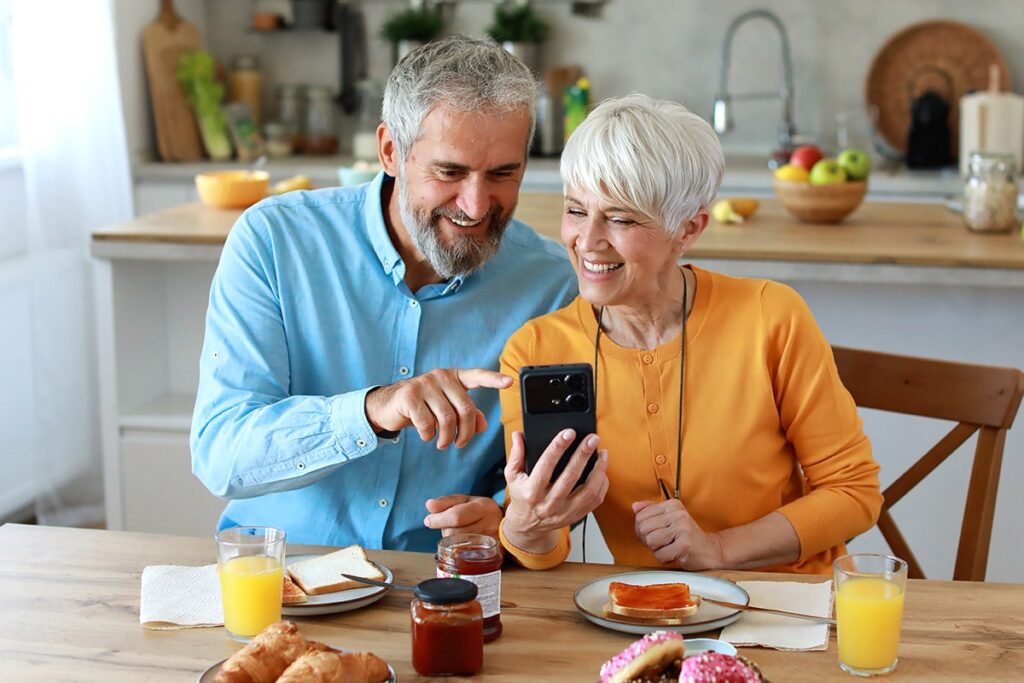 The Gardens at Shadow Hills | Senior Town Homes | Senior Couple Eating Breakfast While Researching On Their Smart Phone